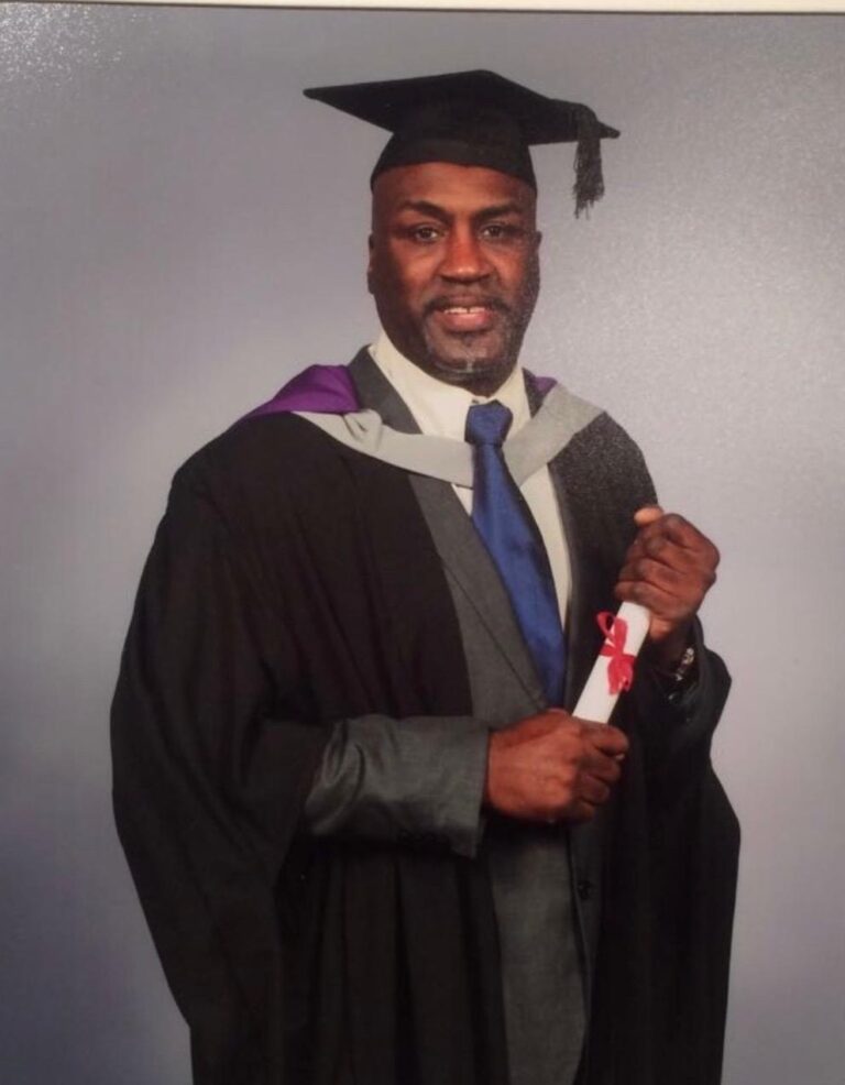 Derek at his graduation in cap and gown, holding a scroll